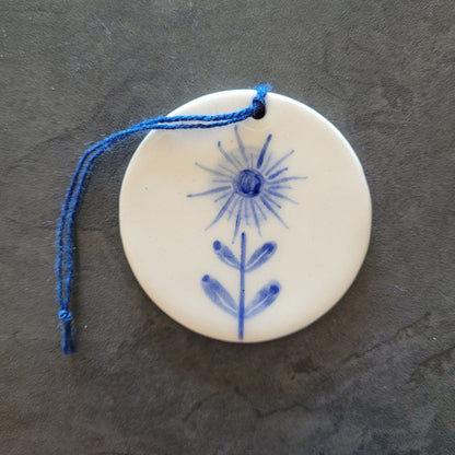Round ceramic ornament with blue floral design and string on a dark surface