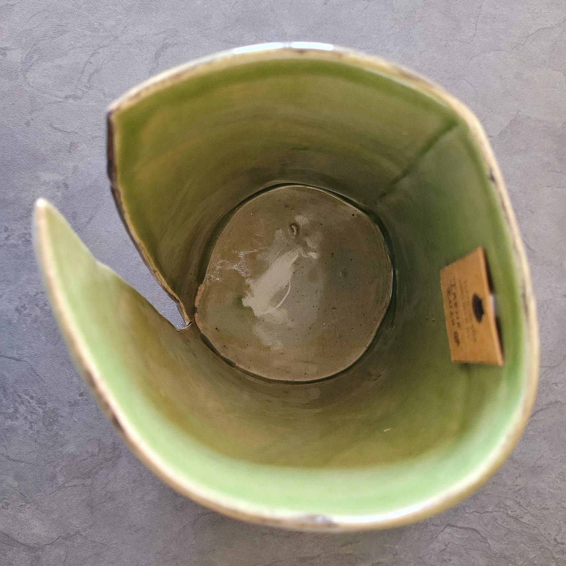 Green ceramic vase with a small brown label on a gray surface