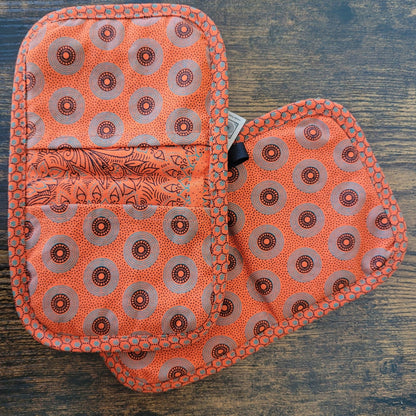 Set of orange patterned pot holders on a wooden surface