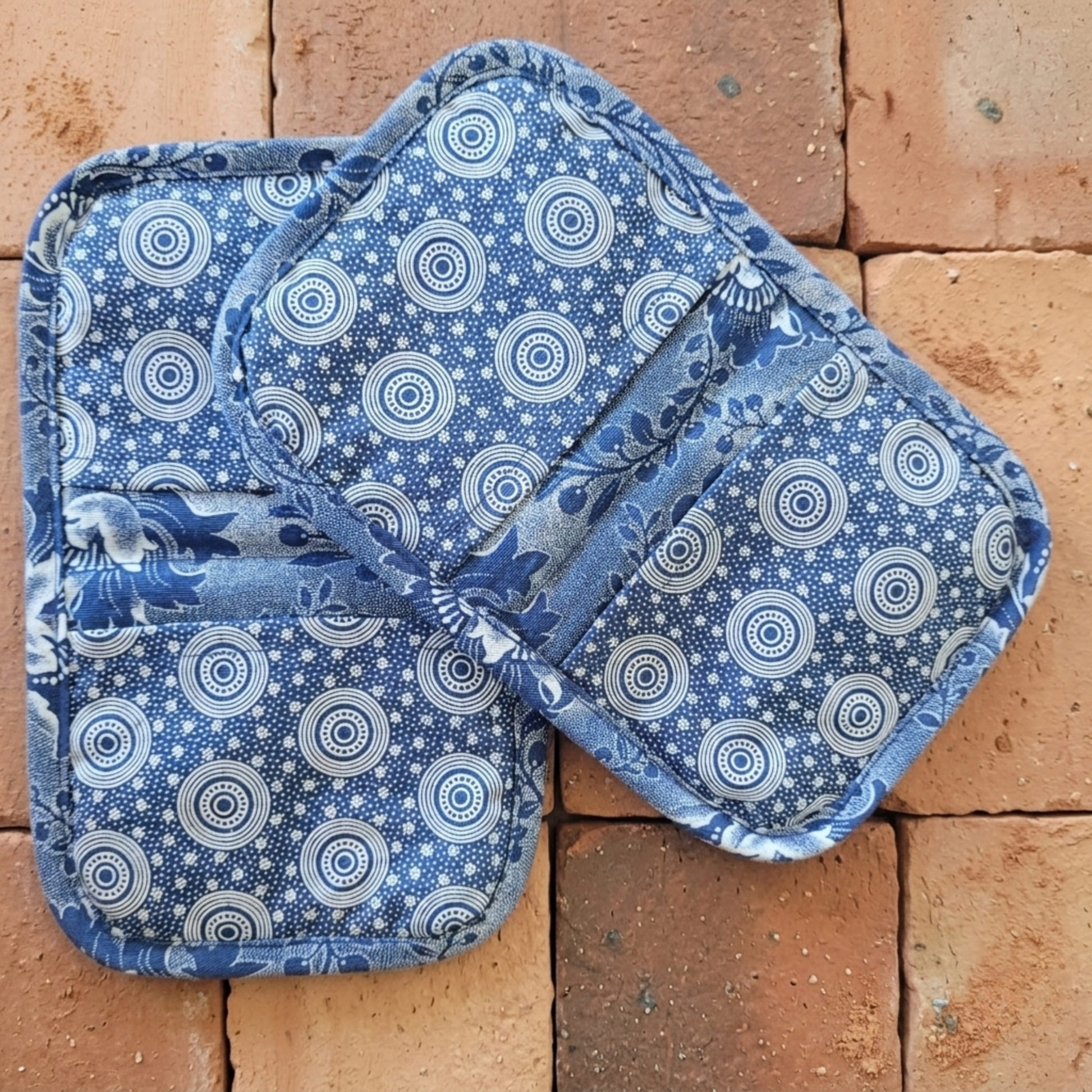 Pair of blue and white patterned pot holders on a brick surface
