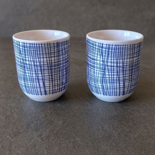 Two white ceramic cups with blue grid patterns on a gray surface