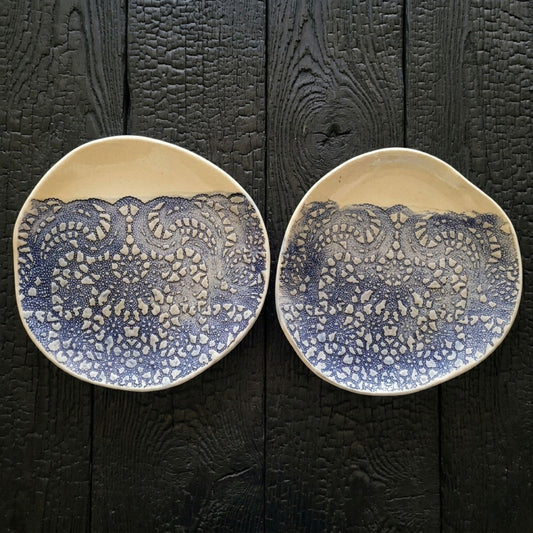 Two ceramic plates with blue lace patterns on a textured black surface