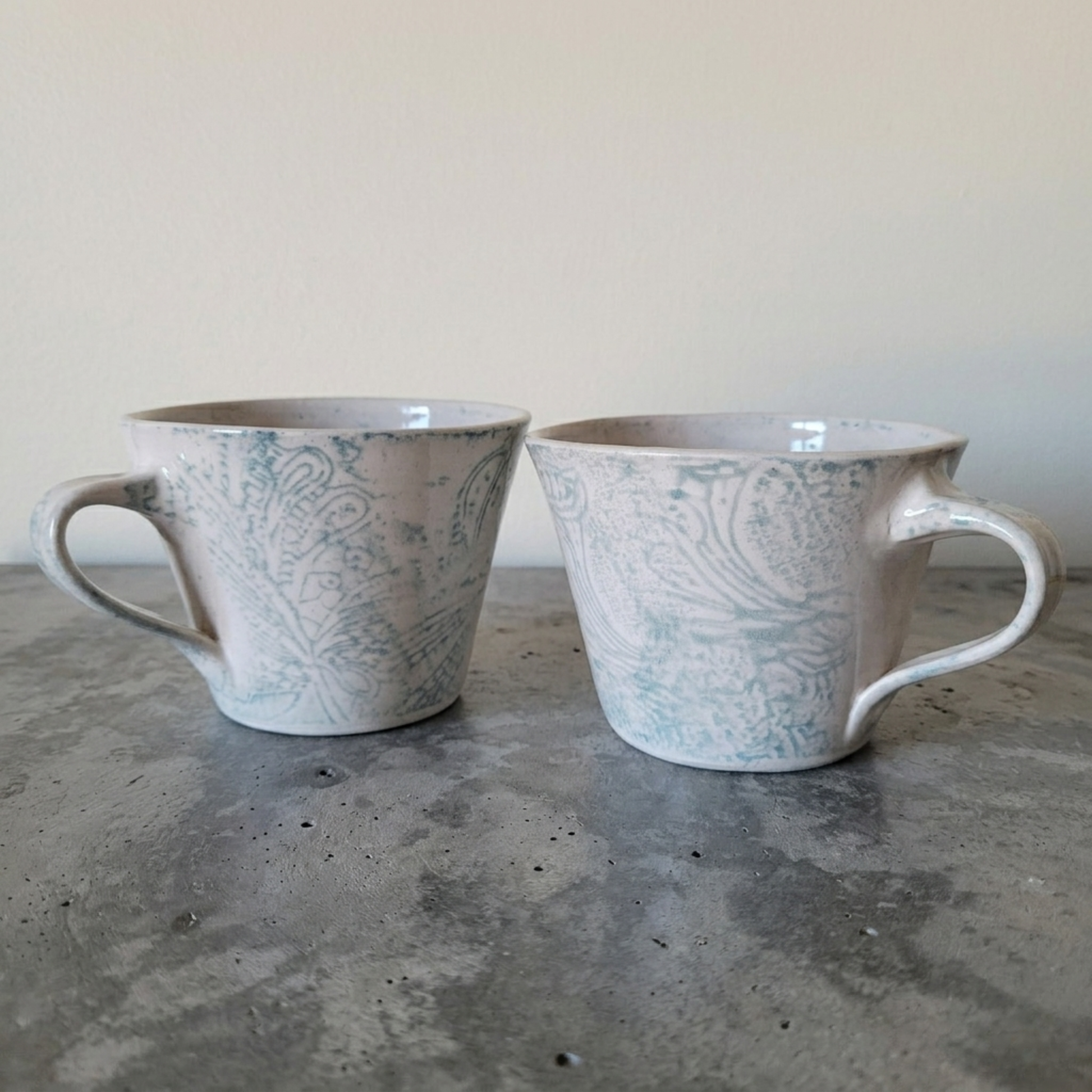 Two ceramic mugs with a paisley pattern on a concrete surface.