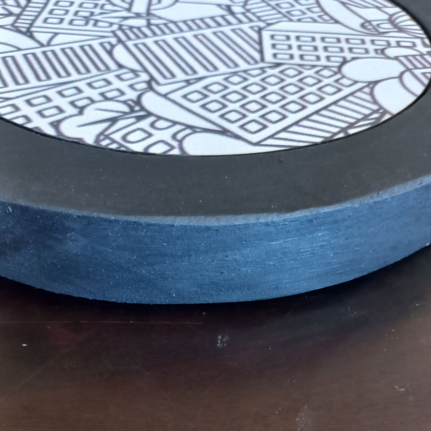 Close-up of a black pot stand with a detailed black and white pattern on a dark surface.