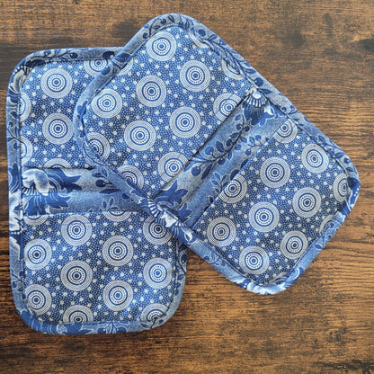 Two blue and white patterned pot holders on a wooden surface