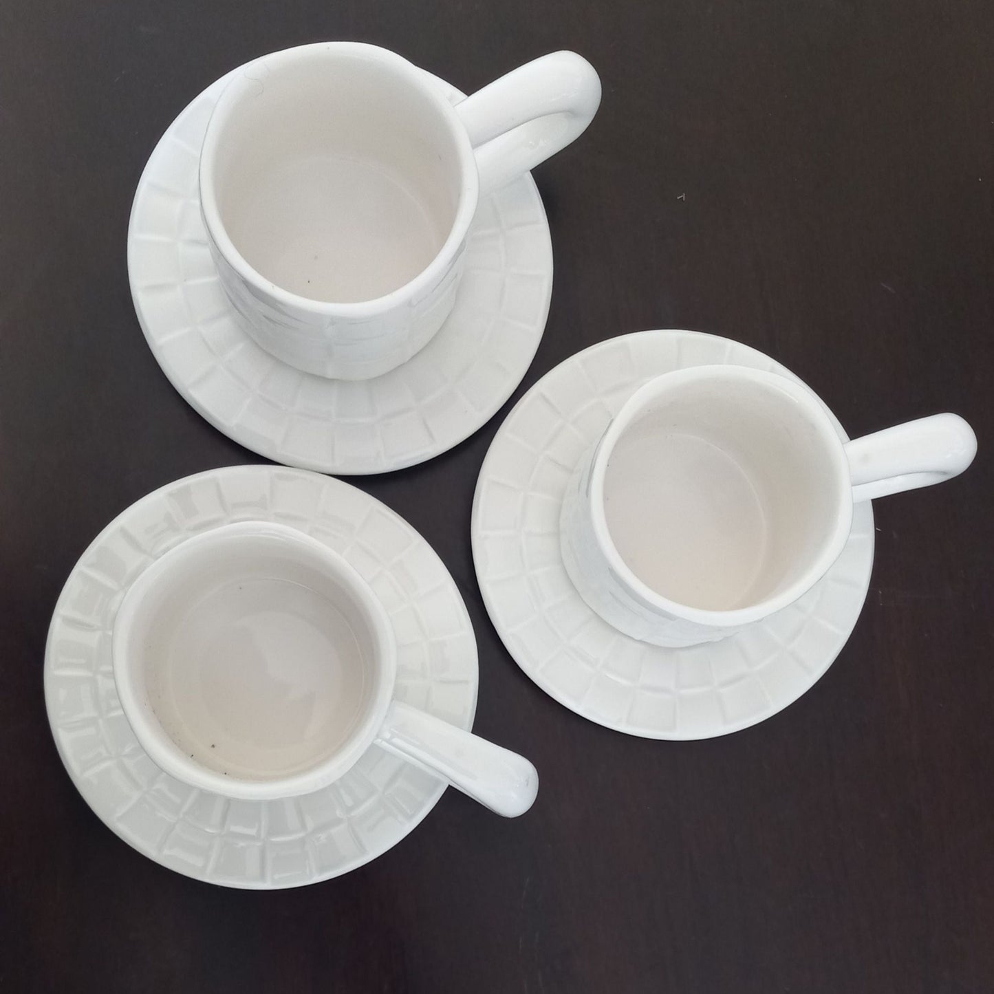 Three white ceramic cups with saucers on a dark background