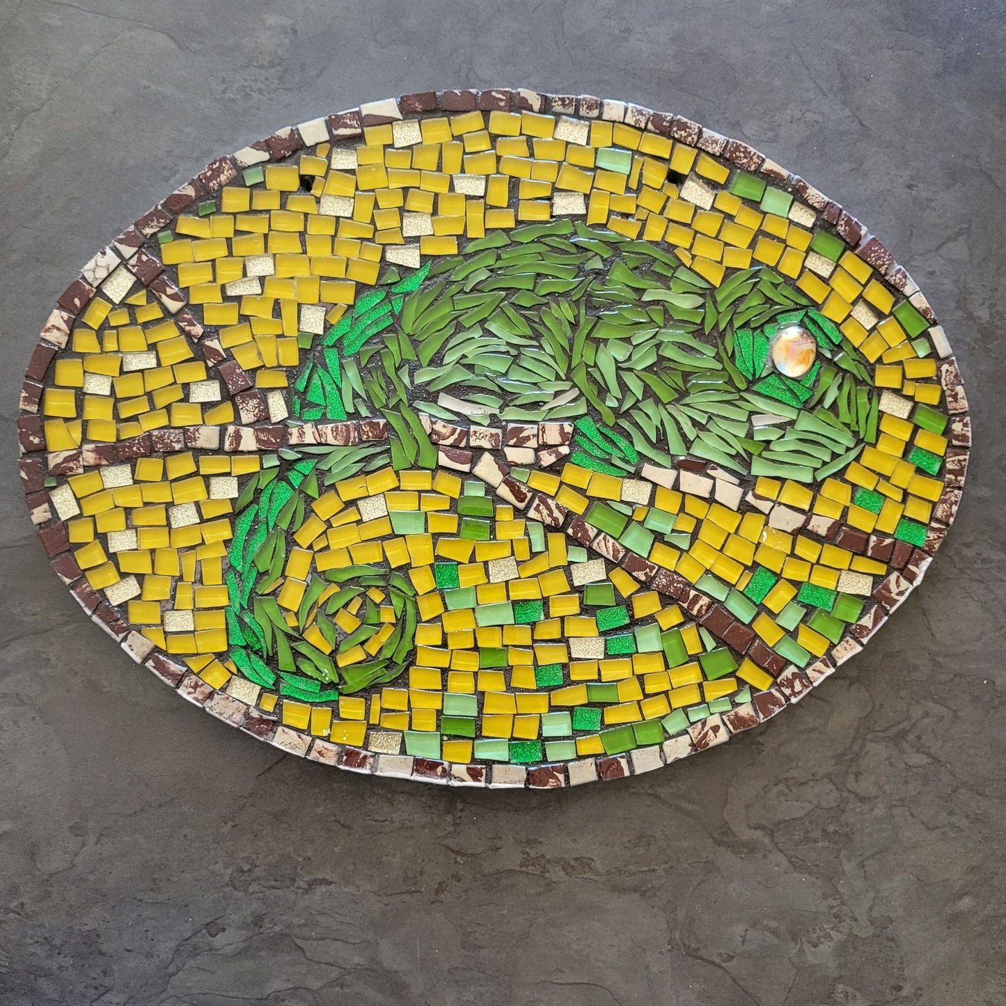 Mosaic artwork of a chameleon on a gray surface