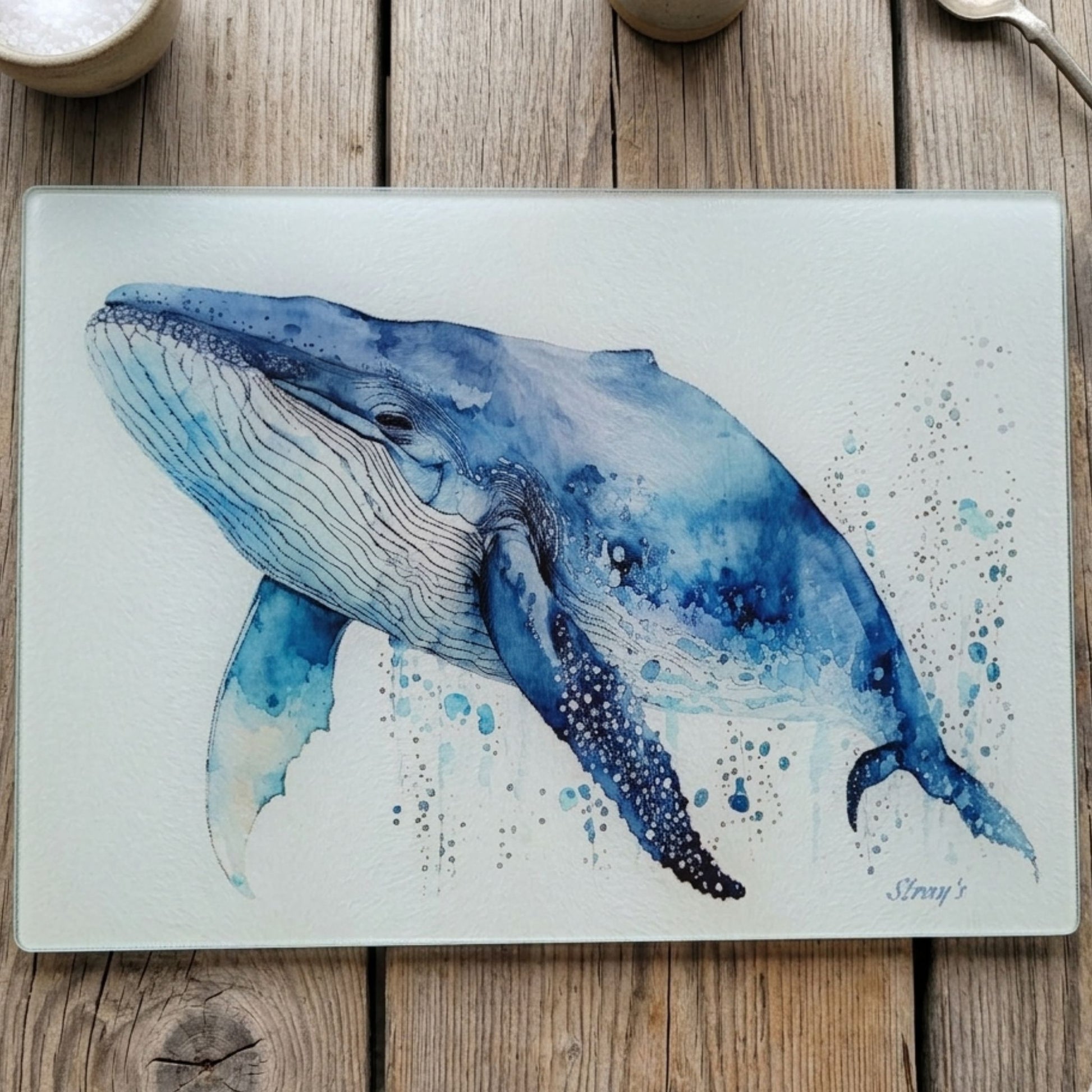 Watercolor print of a whale on a glass cutting board with a wooden background