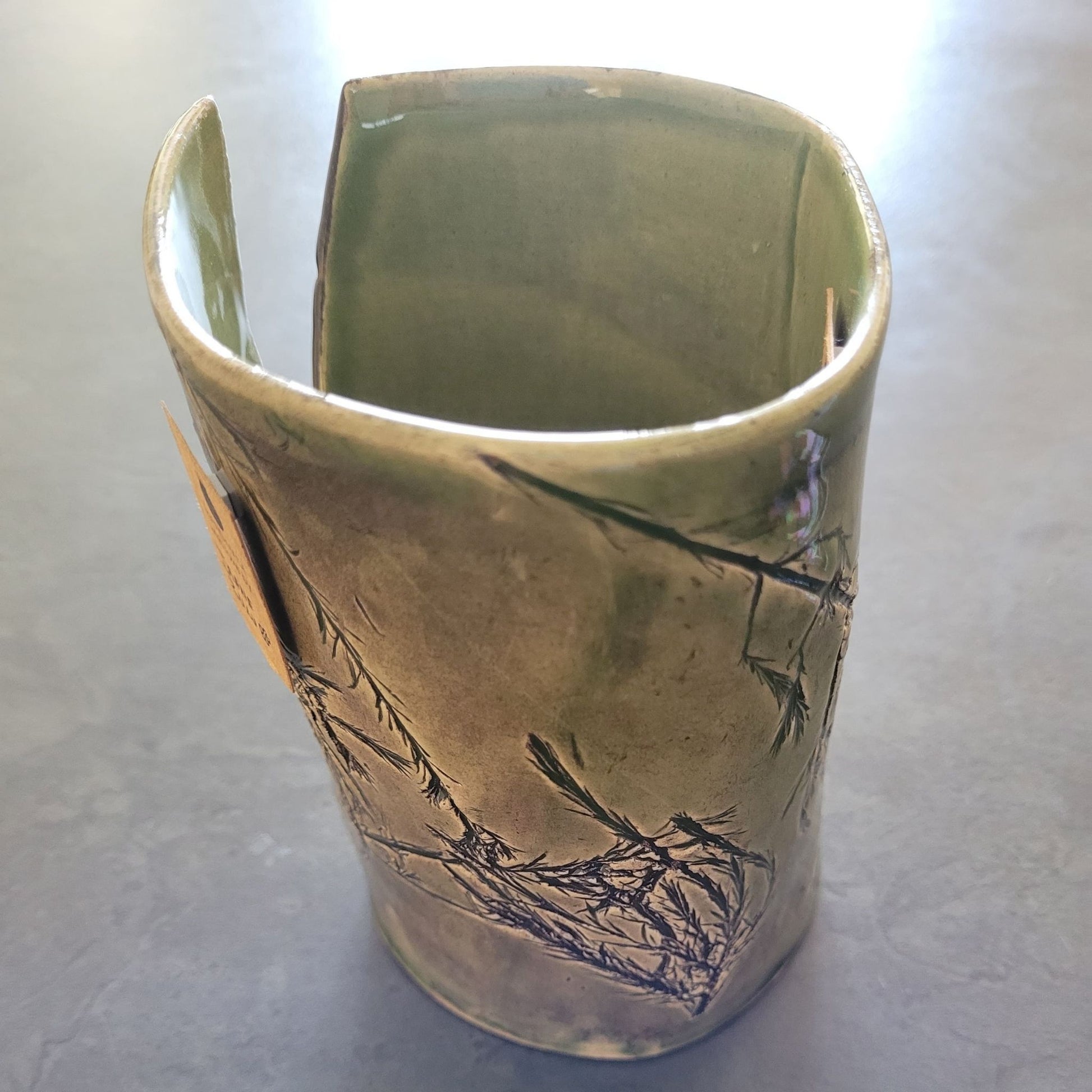 green ceramic vase with leafy imprint on a gray surface