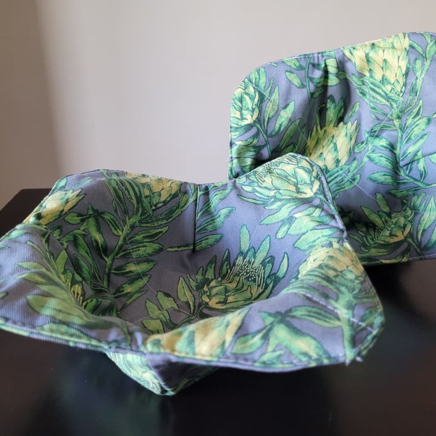 Two fabric bowl cozies with green leaf pattern on a dark surface