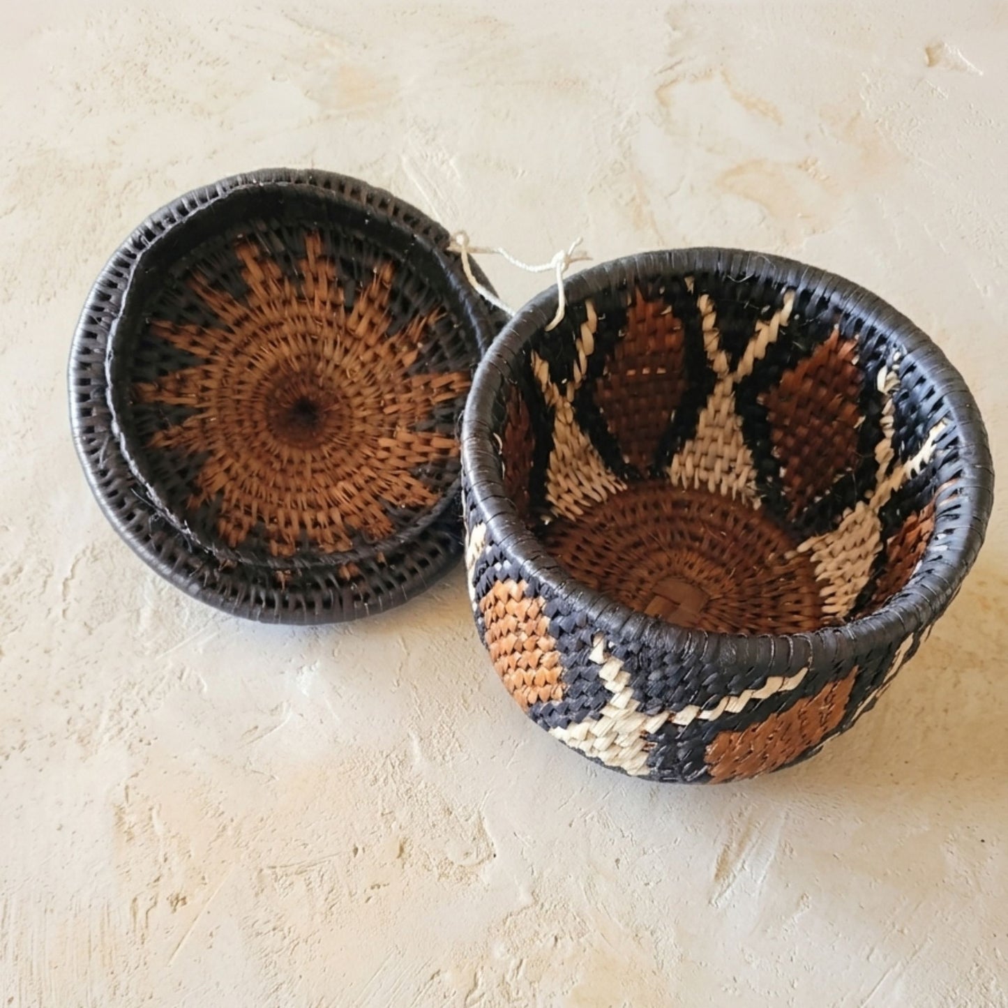 Woven basket and lid with a geometric pattern on a beige surface