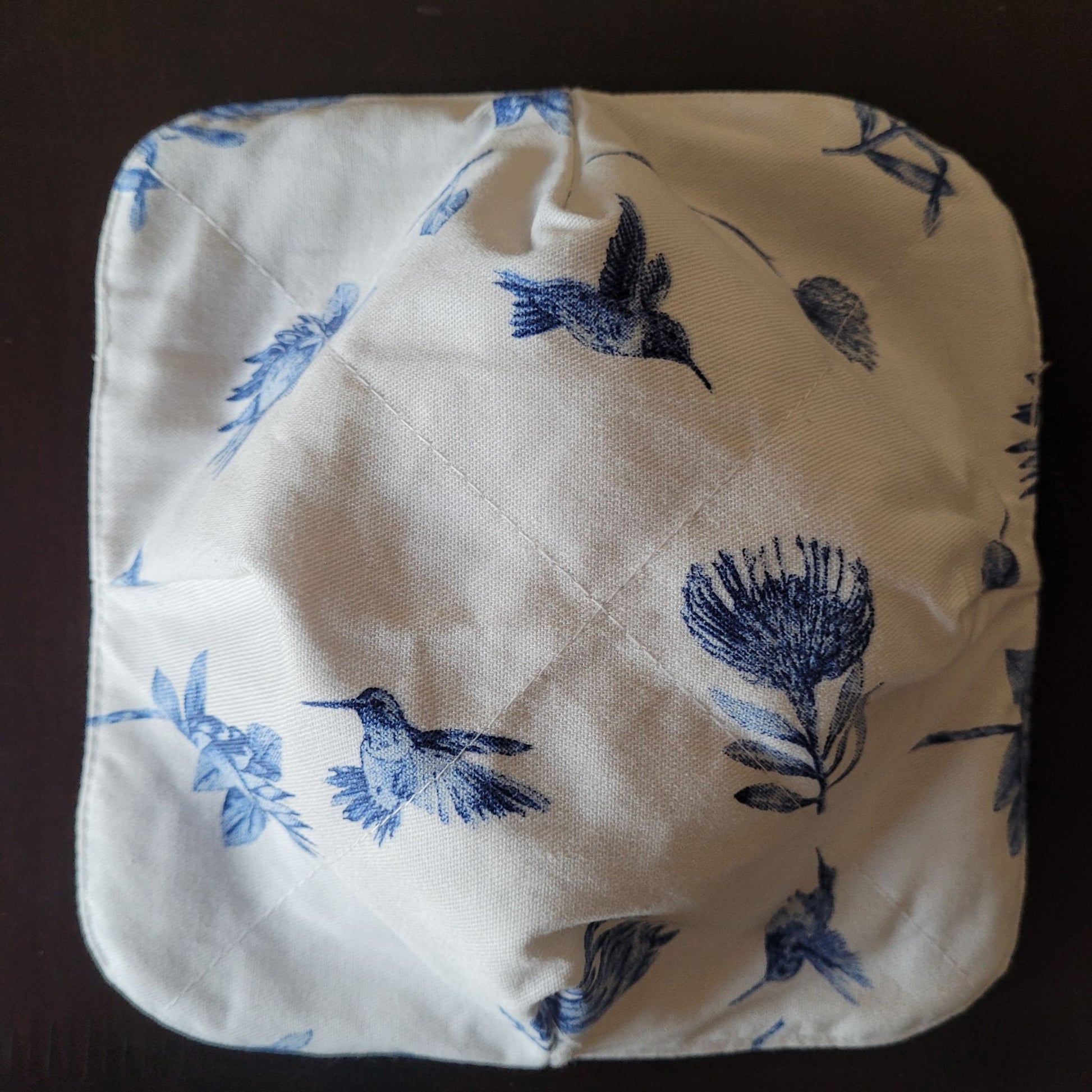 Quilted square hot pad with blue bird and floral pattern on a dark background