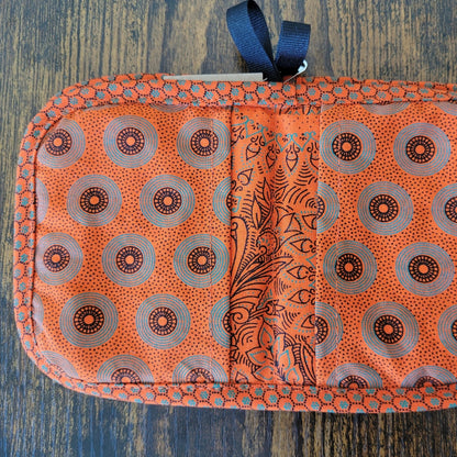Orange pot holders with circular patterns and a blue strap on a wooden surface