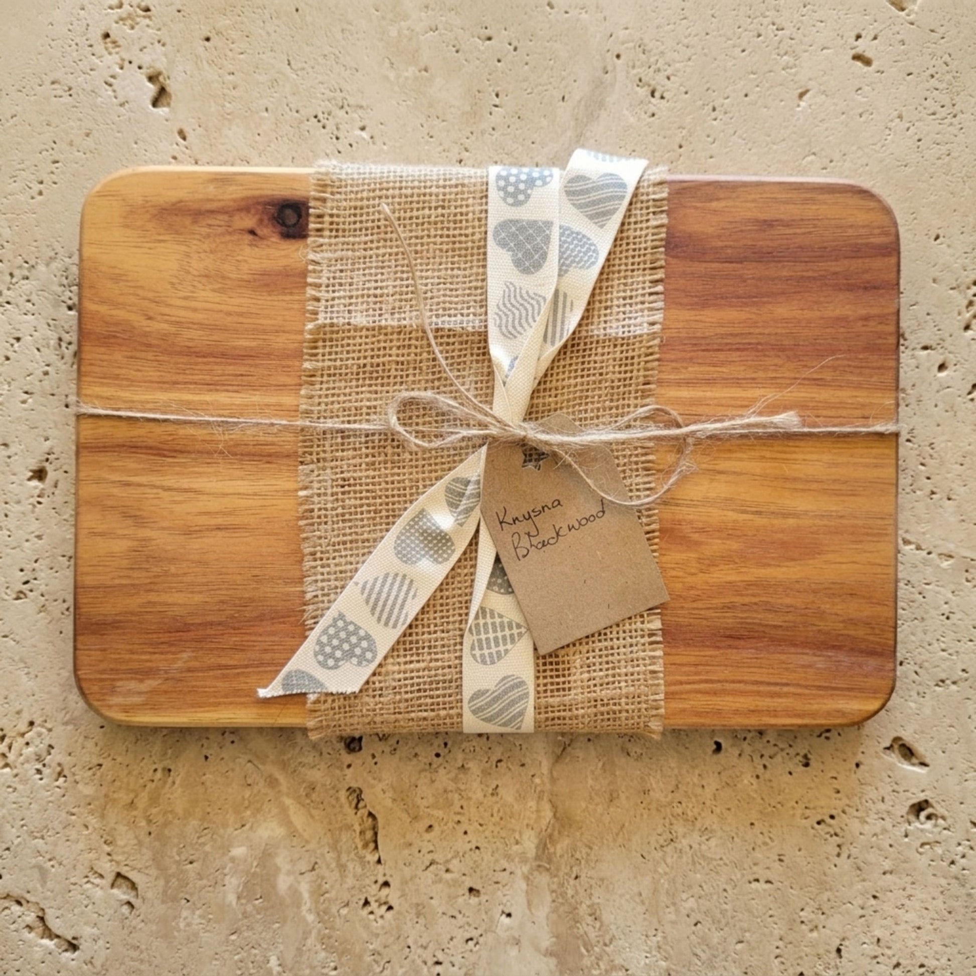 Knysna blackwood cutting board wrapped with burlap and ribbon on a textured surface