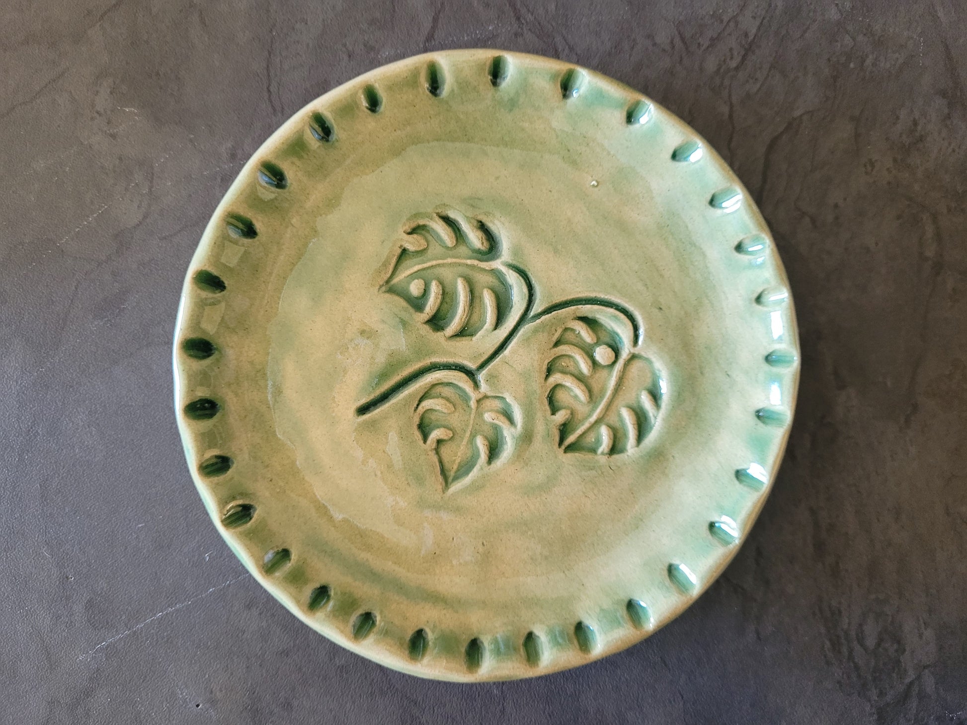 Green ceramic plate with decorative design on a gray background