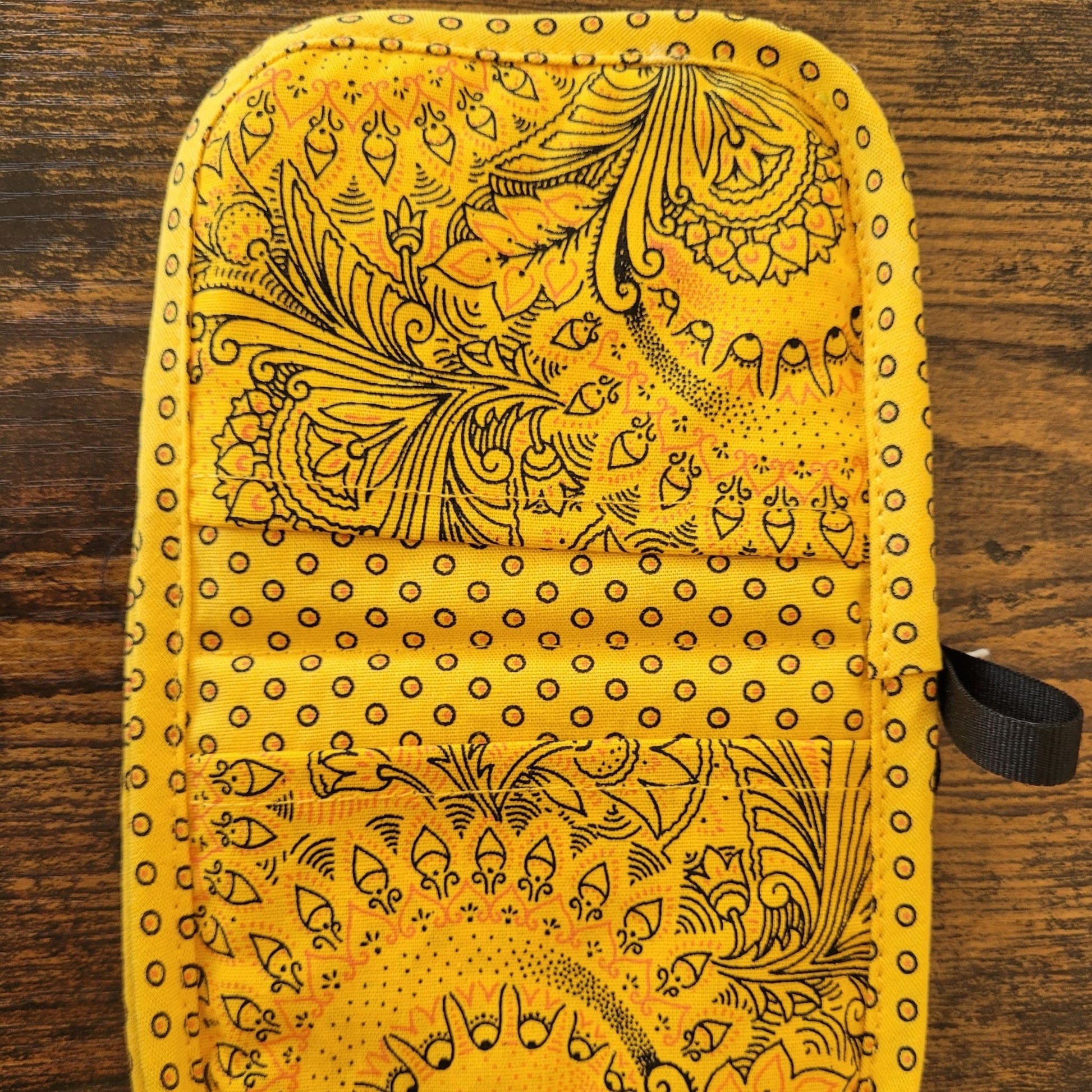 Yellow shweshwe pot holders with black patterns on a wooden surface