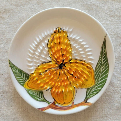 Ceramic grating plate with a yellow flower design on a beige background