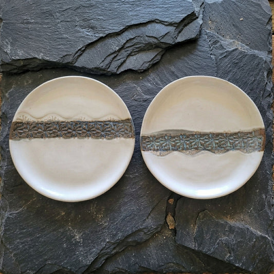Two ceramic plates with decorative edges on a dark stone surface