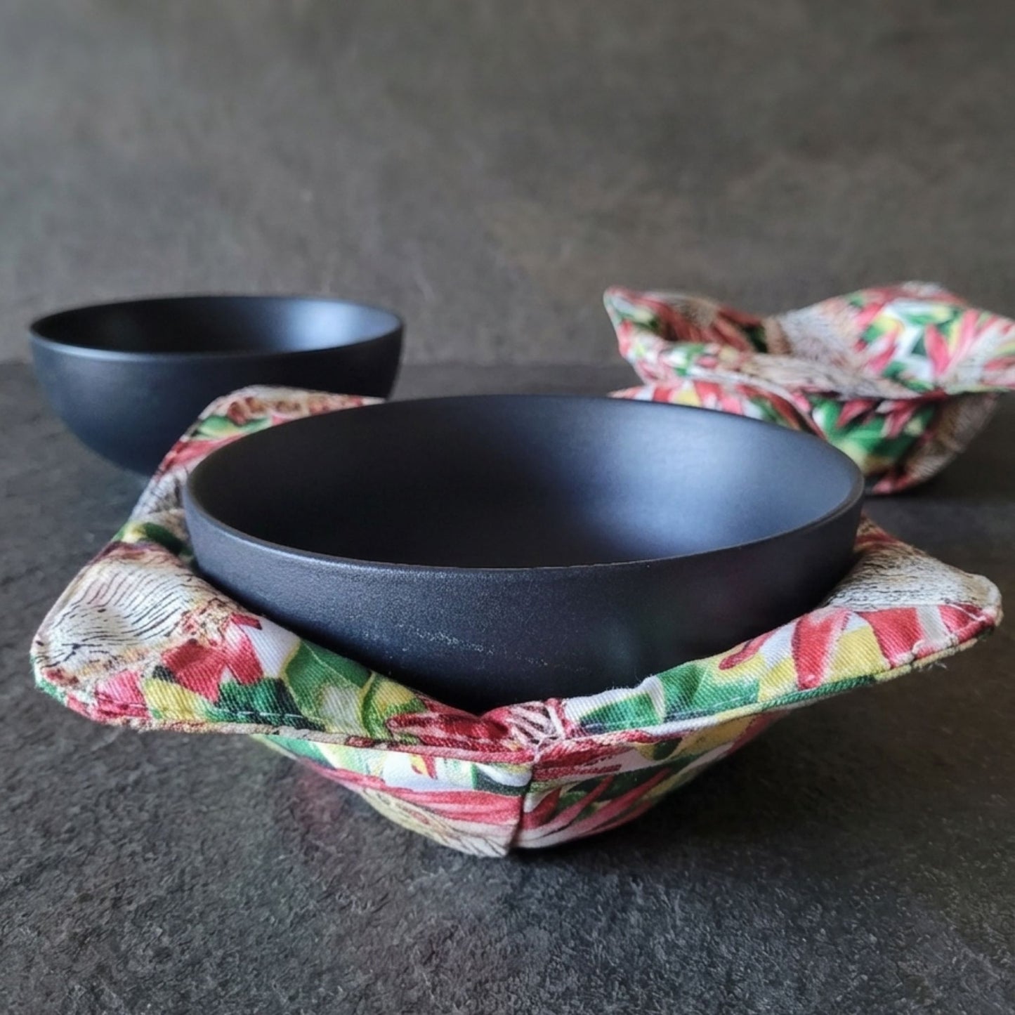 Black bowl in a colorful fabric bowl cozy with another bowl in the background.